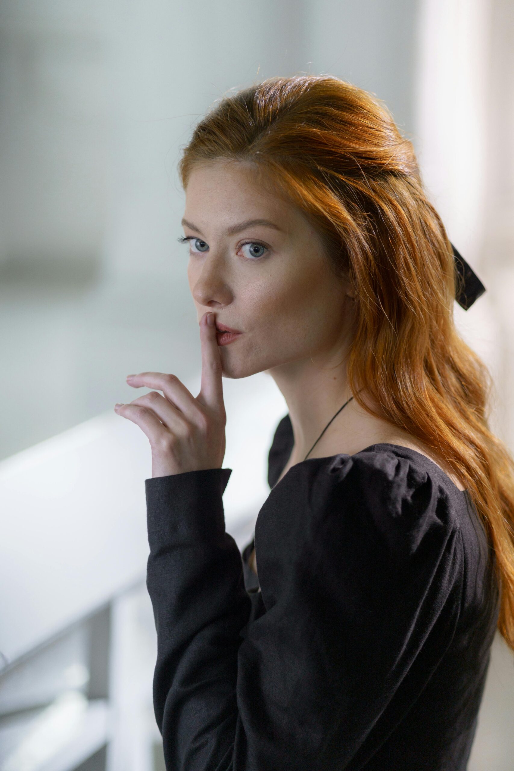 Portrait of a woman gesturing silence with a finger on her lips, wearing a black dress.